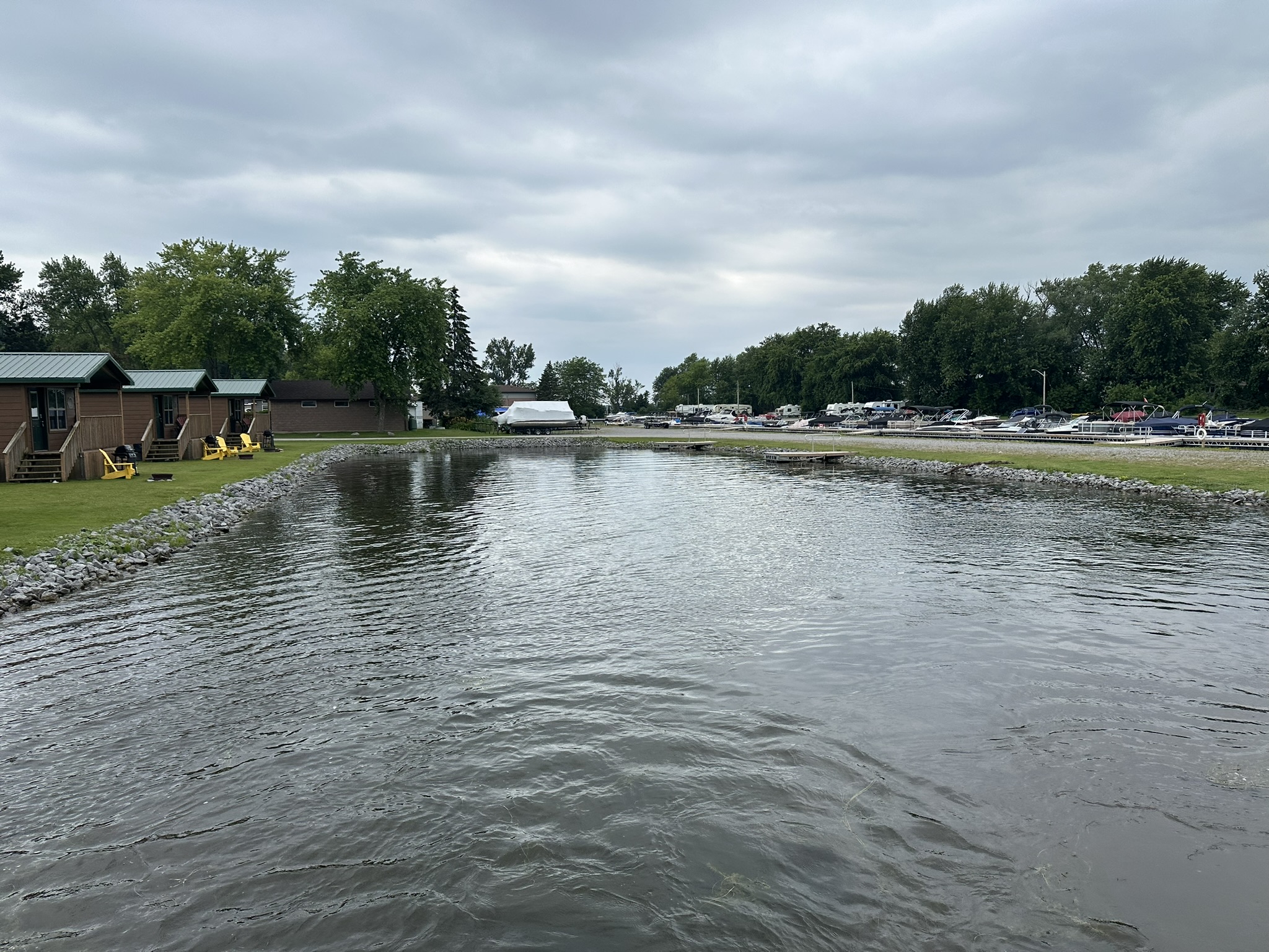 Cottages line a lakeside with green roofs. Parked boats visible in the marina. Overcast sky enhances the serene, natural setting.