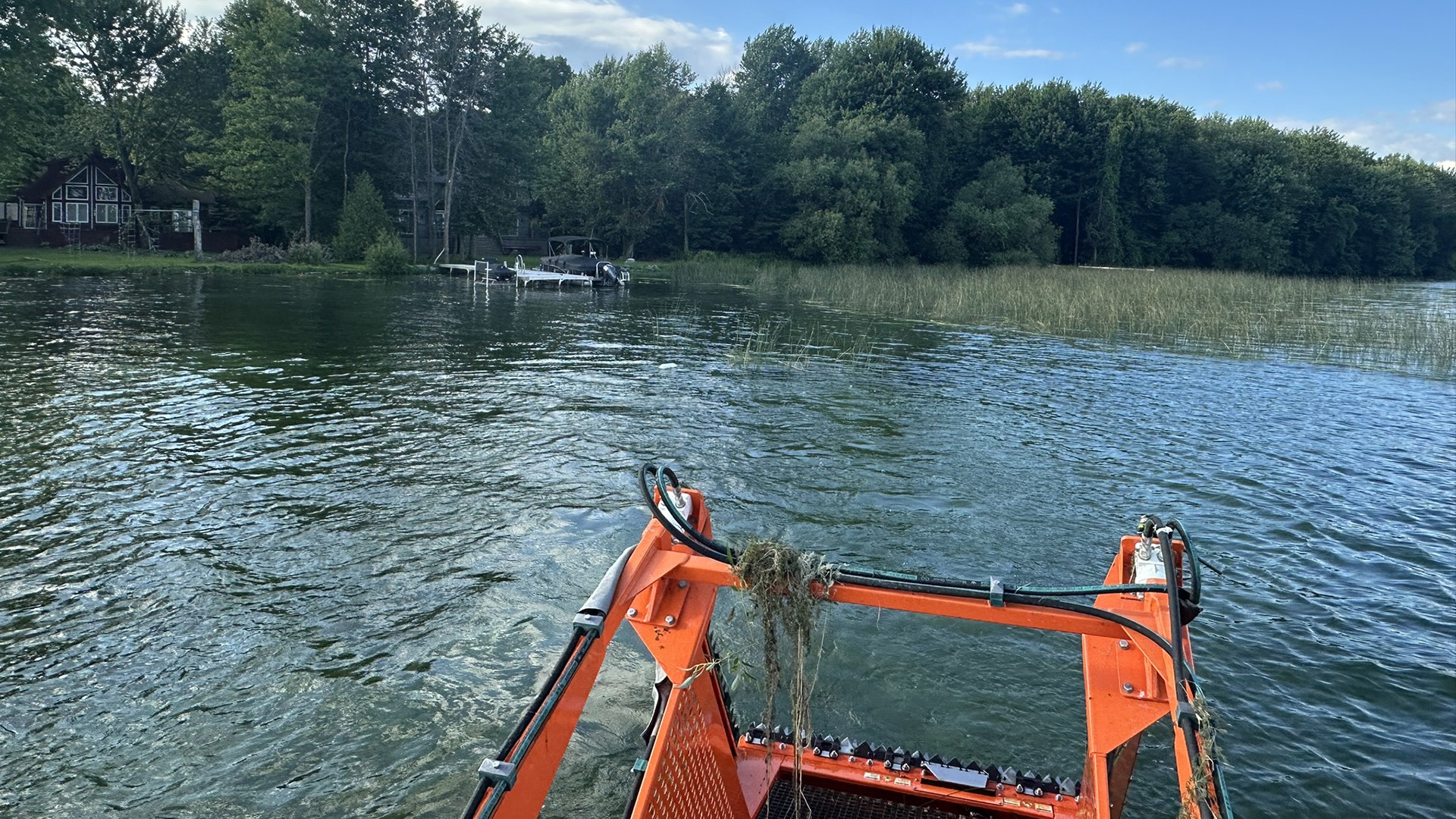 A bright orange aquatic machine on a tranquil lake, surrounded by lush trees and a dock near rustic lakeside cabins.