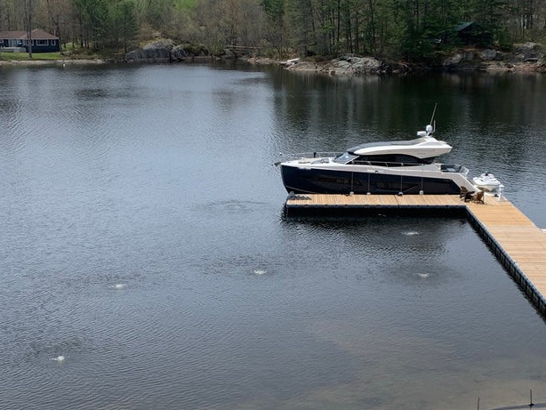 A sleek boat moored at a wooden dock on a calm lake, surrounded by lush trees and rustic cabins in the background.
