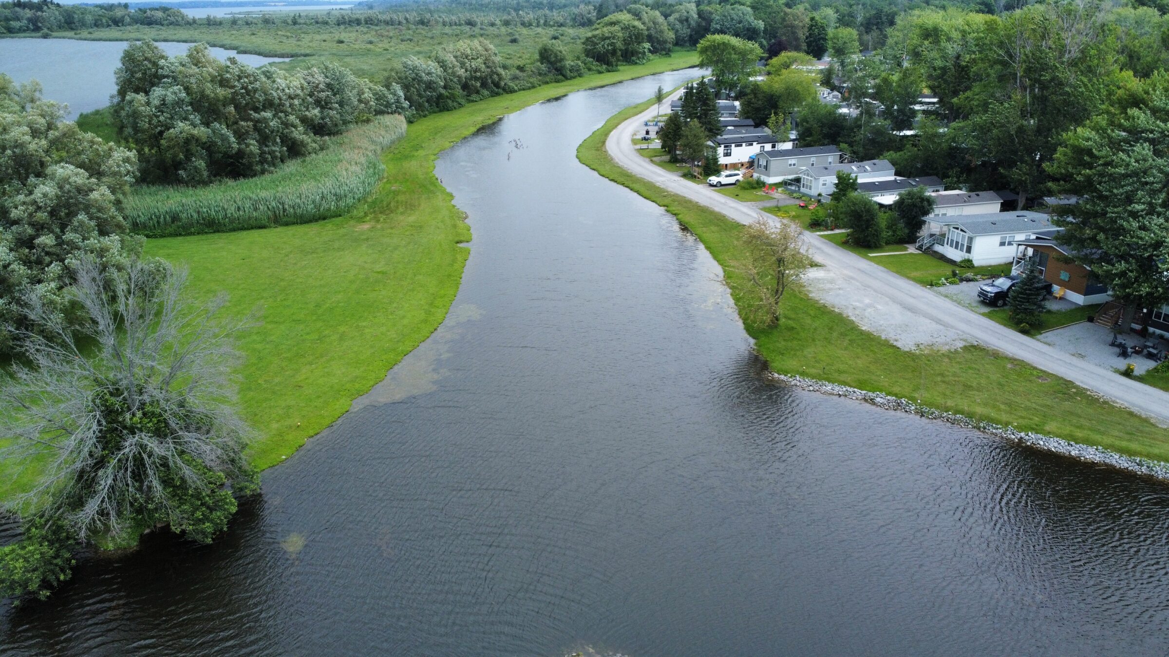 Aerial view of a river winding through a rural area with houses, trees, and lush greenery along the banks.