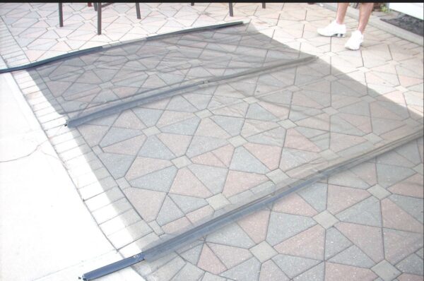 A person stands near a large mesh screen on a patterned stone patio, with table and chair legs visible in the background.