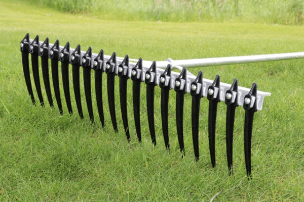 A multi-blade dethatching rake with black tines is placed on green grass, designed for lawn maintenance and debris removal.